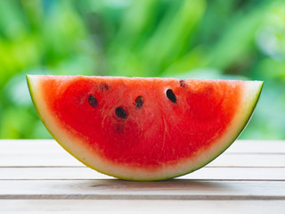 Watermelon sliced on a wooden table with green leaves in the background