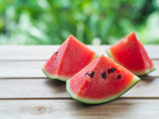 Watermelon sliced on a wooden table with green leaves in the background