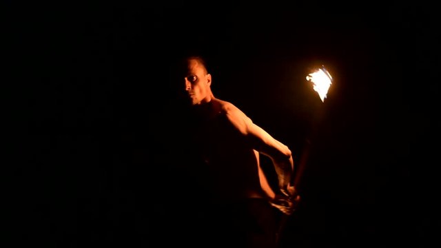 Close-up Slow motion of a young man in black pants in total darkness shows a representation of a rotating burning torch. Meditation in motion. Calm and unwavering. Work with fire. Low key