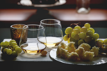 Swiss cheese tete de moine on ceramic board, black and green grapes and two glasses of white wine, served with candle on white table cloth with window behind. Natural day light. Romantic dinner.