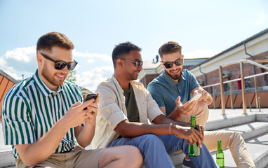 leisure, technology and people concept - happy male friends with smartphones drinking beer and talking on street in summer