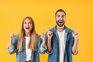 Image of surprised couple pointing fingers upward at copyspace
