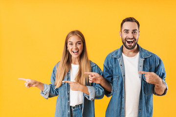 Image of young couple smiling while pointing fingers aside at copyspace