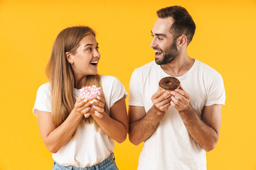 Image of beautiful couple smiling while holding sweet donuts together