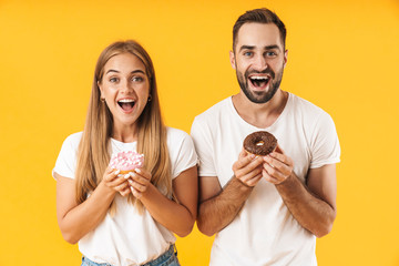 Image of excited couple smiling while holding sweet donuts together