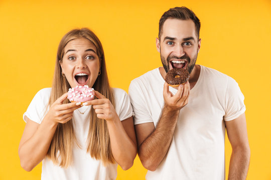 Image of pleased couple smiling while eating sweet donuts together