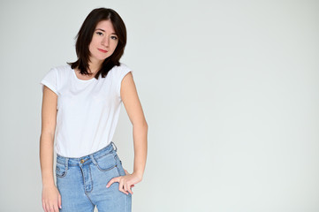 Portrait of a pretty asian brunette girl with black hair in a white t-shirt and blue jeans on a white background. It stands right in front of the camera, with emotions in various poses.