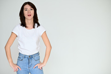 Portrait of a pretty asian brunette girl with black hair in a white t-shirt and blue jeans on a white background. It stands right in front of the camera, with emotions in various poses.