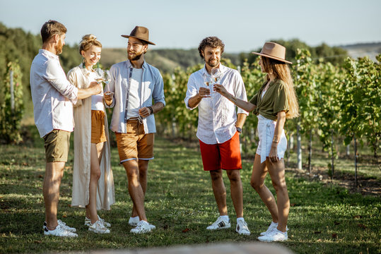 Group of young friends dressed casually hanging out together, tasting wine on the vineyard on a sunny summer morning