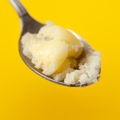 Spoon with Ghee oil closeup on a colored yellow background. Keto diet, Ayurveda