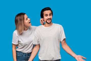 Young blond woman jokingly redukes her brunet bearded boyfriend with mustaches in white t-shirts and blue jeans isolated over blue background.