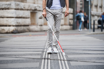 Midsection of young blind man with white cane walking across the street in city. - obrazy, fototapety, plakaty