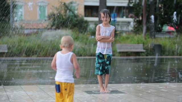 Cute toddler boy and older brothers, playing on a jet fountains with water splashing around, summertime