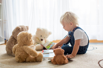 Little toddler boy, reading a book to his teddy bear friends at home