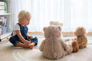 Little toddler boy, reading a book to his teddy bear friends at home