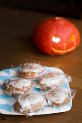 Pumpkin craft homemade glazed cookies on plate on wooden table next to the pumpkin Jack-o'-lantern in autumn of October for the All Saints' Eve Halloween party. Sweets for children for Trick or treat