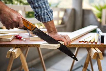 Adult craftsman carpenter with manual saw working on cutting a wooden table. Housework do it yourself. Stock photography.
