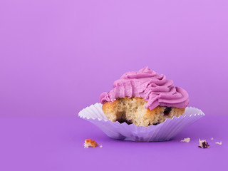 Blueberry cupcake with buttercream frosting, bite missing and crumbs on table, horizontal image
