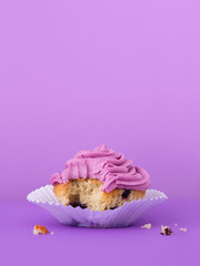 Blueberry cupcake with butter cream frosting, bite missing and crumbs on table, vertical image