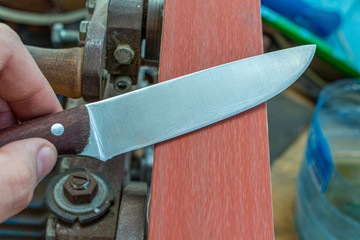 sharpening polishing kitchen knife blade on the belt grinder sander equipment. Knife making.