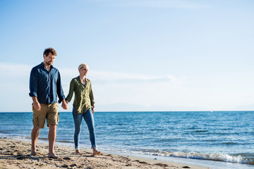 Young couple walking outdoors on beach, holding hands. Copy space.