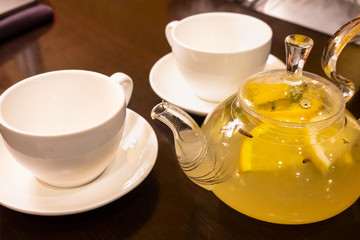 A Cup of green tea with slices of lemon and a kettle of hot tea on the table.