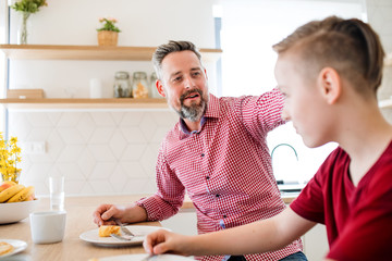 Mature father with small son indoors sitting at the table, eating pancakes.