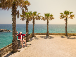 Christmas Santa Claus relaxing on a sandy beach under palm trees. Happy new year travel destinations in hot countries concept..