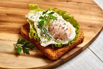 Poached egg, benedict on toasted white bread toast with salad and spices on a wooden background.