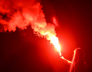 Red smoke bomb in a girl’s hand at night