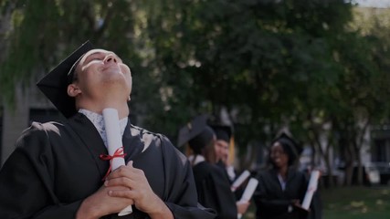 Successful caucasian male graduate with high degree level proud of his diploma at graduation. He excited, shows diploma and looking in to the camera. Close up. Students on the background.
