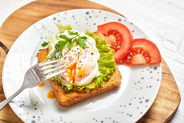 Fototapeta na wymiar Poached egg, benedict on toasted white bread toast with salad and spices on a plate on a light wooden background.