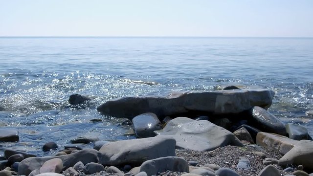 Coastal line of sea beach with huge cobblestones and waves at sunny day. Clear warm weather on sea coast and clear sky over sea water surface.