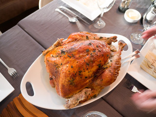 A large home made mouthwatering oven roasted whole turkey with spice rub with breast side up placed on a white serving platter and set table for Thanksgiving dinner celebration with family.
