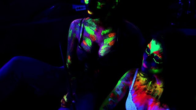 Club party. Sexy young glamorous girls with neon paint relaxing in nightclub and smoking hookah