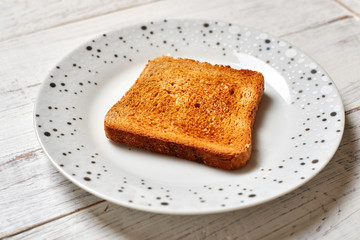 Toasted white toast on a plate on a light wooden background.