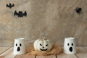Front view of Halloween pumpkins, White pumpkins ghost and paper cup ghost on cement wall background., Bat and spider background with copy space for text. Halloween concept.
