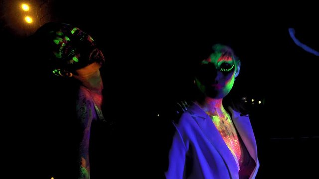 Two women with glowing fluorescent bodyart looking at camera