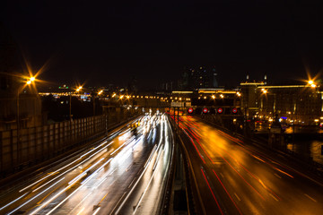 Panoramic view on a city highway with glowing lines of light from headlamps and architecture against the night dark sky