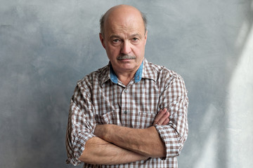 Middle aged hispanic man with doubtful expression and arms crossed looking at camera. Studio shot