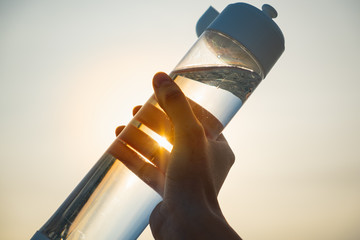Human hand holds a water bottle against the setting sun. Close up of a reusable water bottle in a...