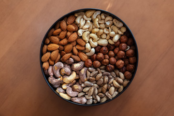 Hazelnuts, almonds, raw cashews, fried cashews and pistachios in plate on wooden table.