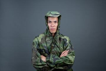 The young man wears a camouflage raincoat and shows different gestures. On a gray background in the...