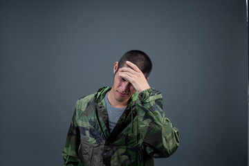 The young man wears a camouflage raincoat and shows different gestures. On a gray background in the...