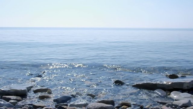 Coastal line of sea beach with huge cobblestones and waves at sunny day. Clear warm weather on sea coast and clear sky over sea water surface. Seascape background.