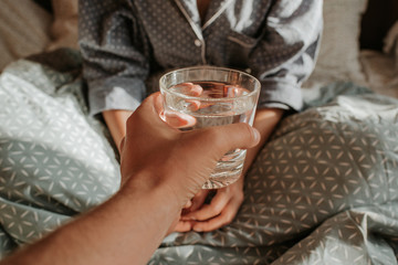 Woman in bed holding a glass of water in hand. Happy morning. Girl in pajamas. Healthy lifestyle, wellness. Proper nutrition. Drinking water. Morning with water. Sunlight on linens. Pillow, blanket