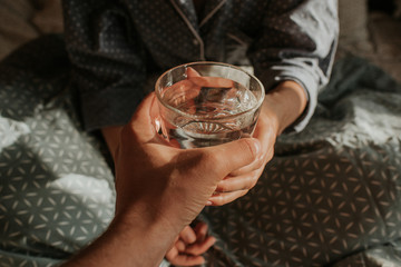 Woman in bed holding a glass of water in hand. Happy morning. Girl in pajamas. Healthy lifestyle, wellness. Proper nutrition. Drinking water. Morning with water. Sunlight on linens. Pillow, blanket