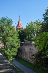 Tower Tiergärtnertorturm with high city wall, lower bastion and moat and southern castle garden, in the background the Nuremberg castle with white and blue Bavaria flag on a tower