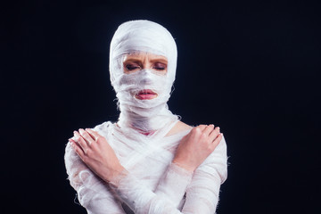 Glamorous mummy woman in bandages all over her body in studio black background. Halloween party or plastic surgery victim concept