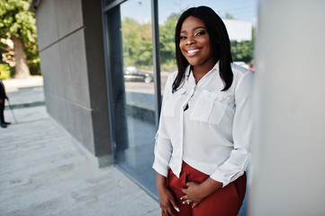 Formally dressed african american business woman in white blouse and red trousers. Successful dark skinned businesswoman.
